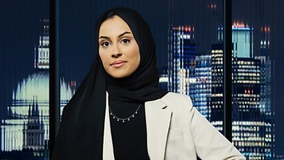 A woman in a suit looks to camera (Rothna Akhtar) as a city landscape shows in the background 