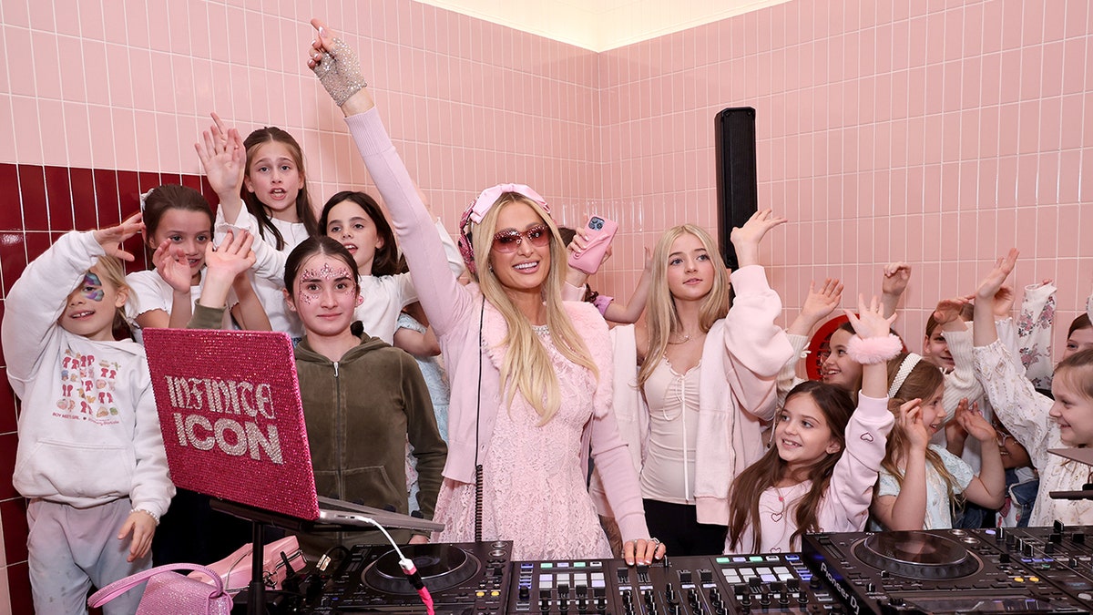 Paris Hilton DJing with a group of smiling girls.