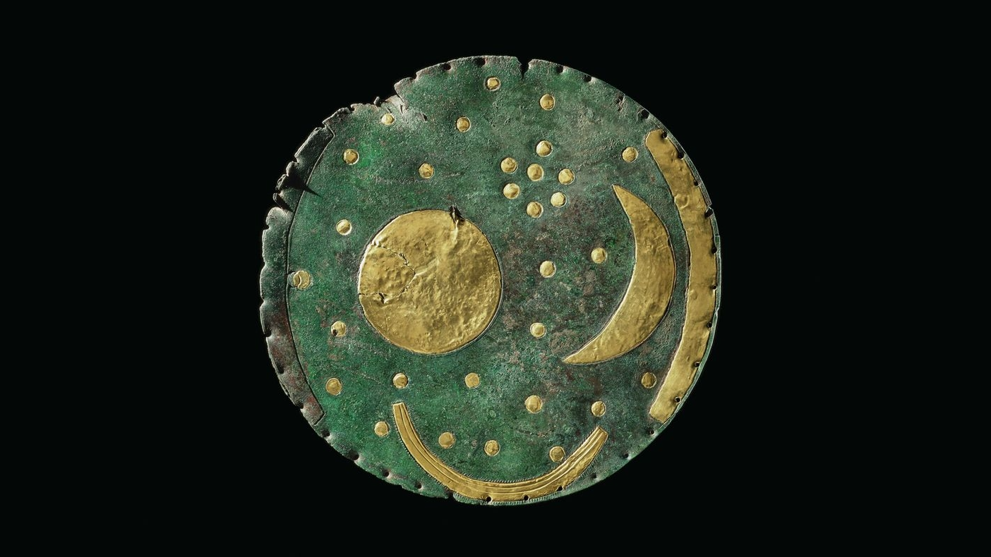 a green-patinaed bronze disk with gold accents representing a crescent moon, sun, and boat