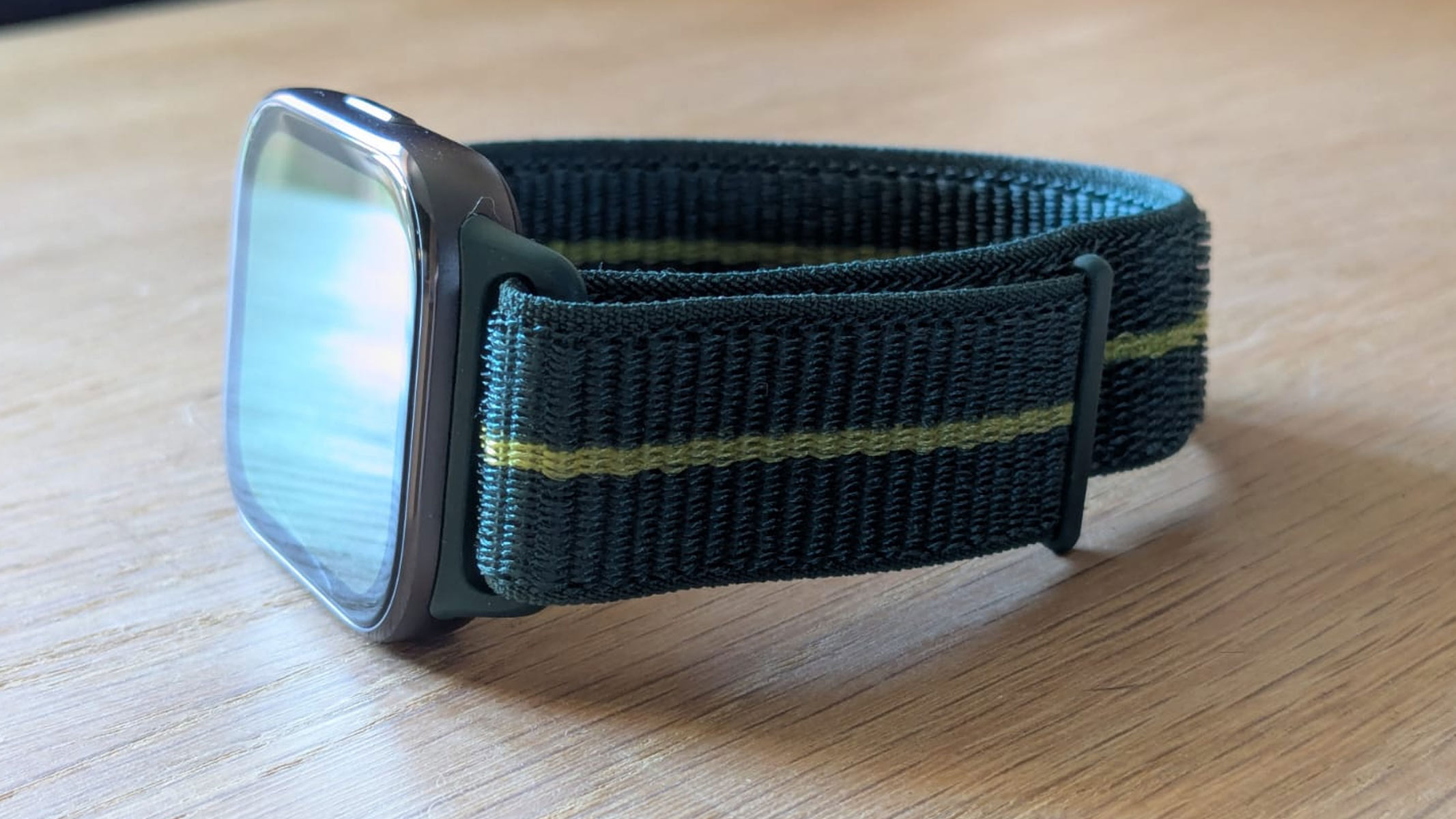 The Motorola Moto Watch Fit on a wooden table, showing the Velcro strap.