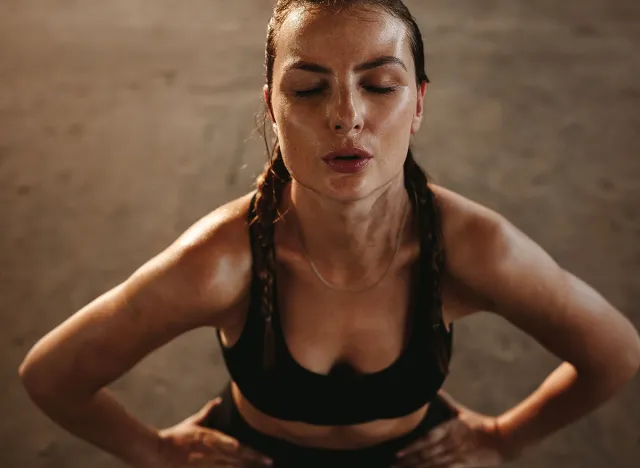 Fit woman with her hands on her hips taking deep breathe. Female athlete taking break after intense workout.