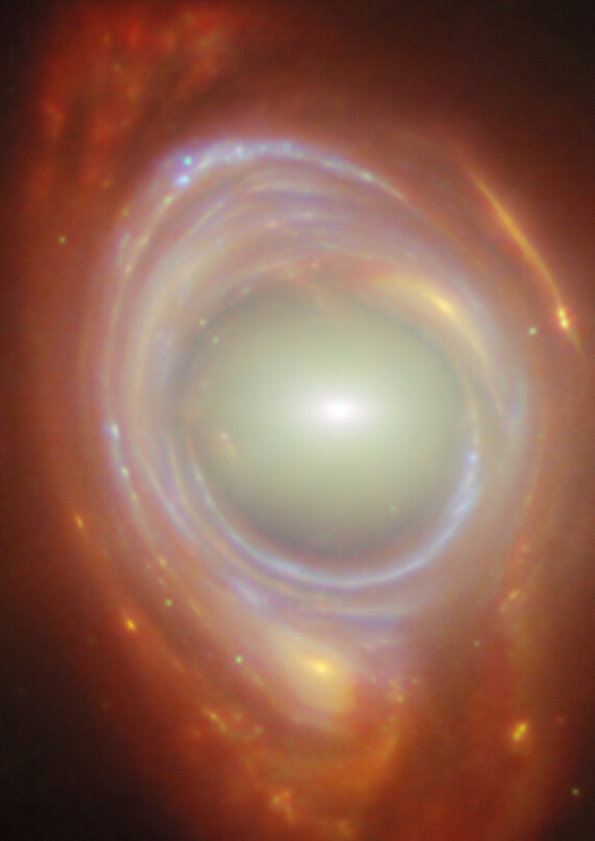 A close-up image of a galaxy with a bright core surrounded by glowing rings of gas and dust, in vibrant red, orange, and blue hues—an awe-inspiring scene that the JWST reveal brings to our universe.