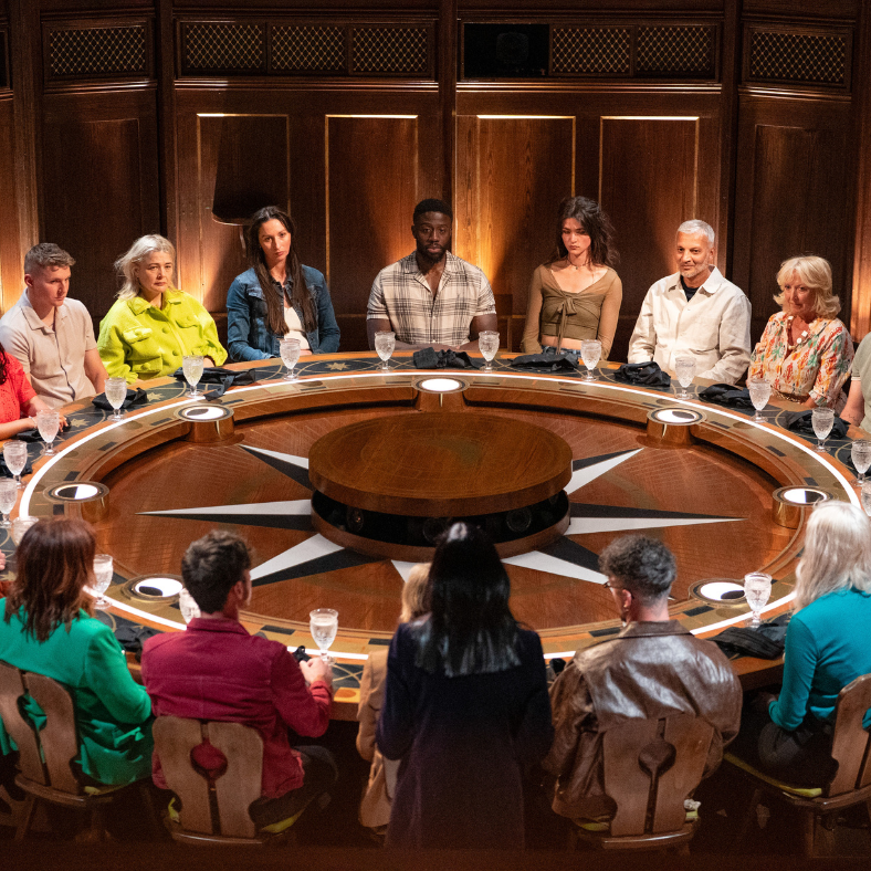 group of people seated around a large circular table in a dimly lit room