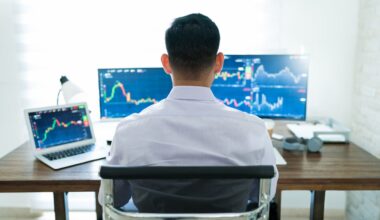 Backside view of an investor or analyst looking at charts on multiple monitors.