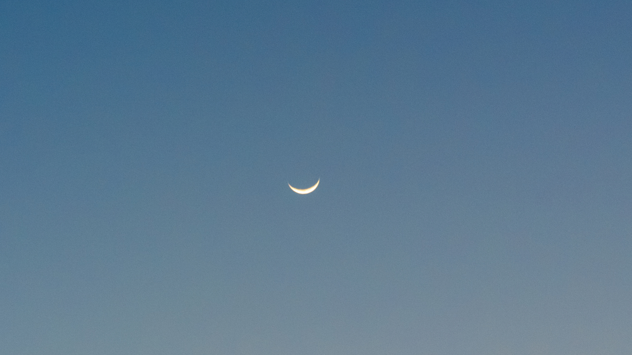 A photo of the pale evening sky showing an upturned crescent moon close to a white star.