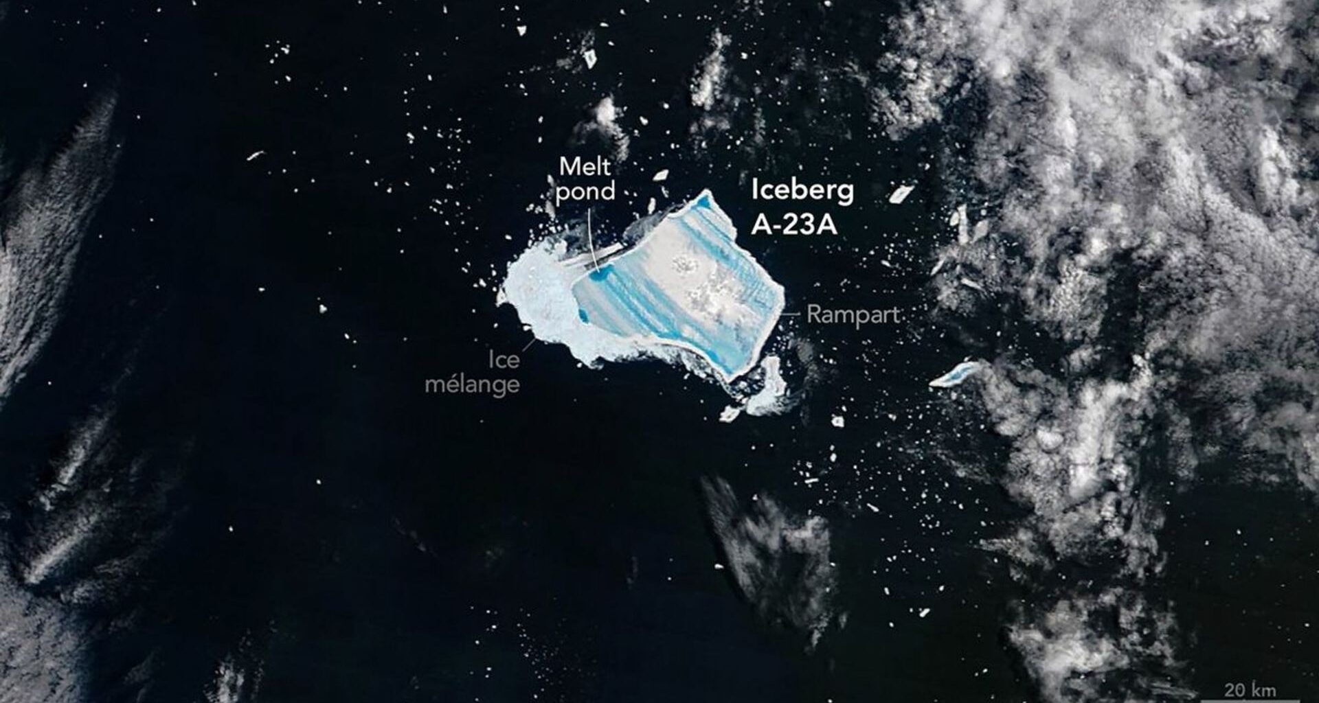 A blue jagged shape is seen in dark waters with white foam from the sea with the large white label Iceberg A-23A next to the blue shape