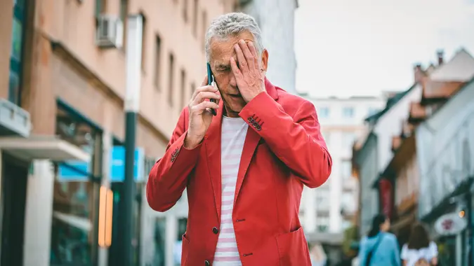 Low angle front view close-up of Caucasian man in early 60s learning bad news as he pauses to take an outdoor call during city break in Ljubljana.