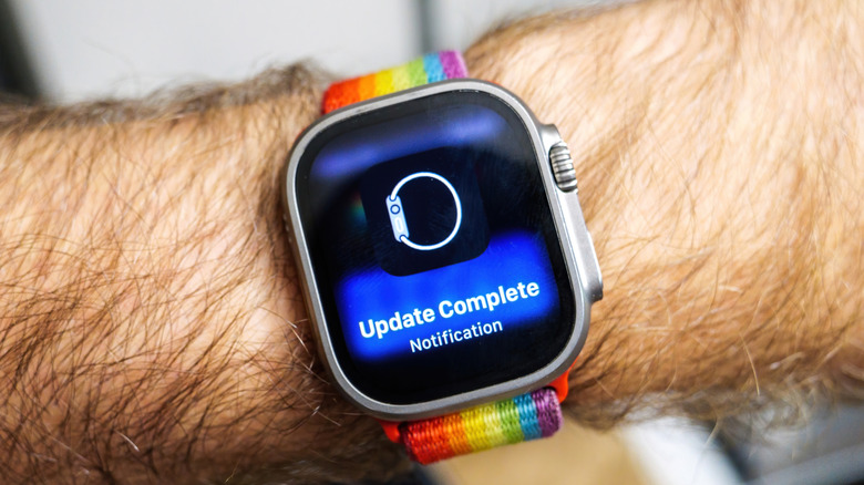 An Apple Watch on a man's wrist with a rainbow band showing an Update Complete notification