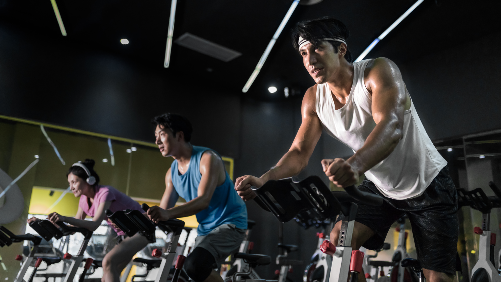 Young people riding stationary bike during indoor cycling class in gym.