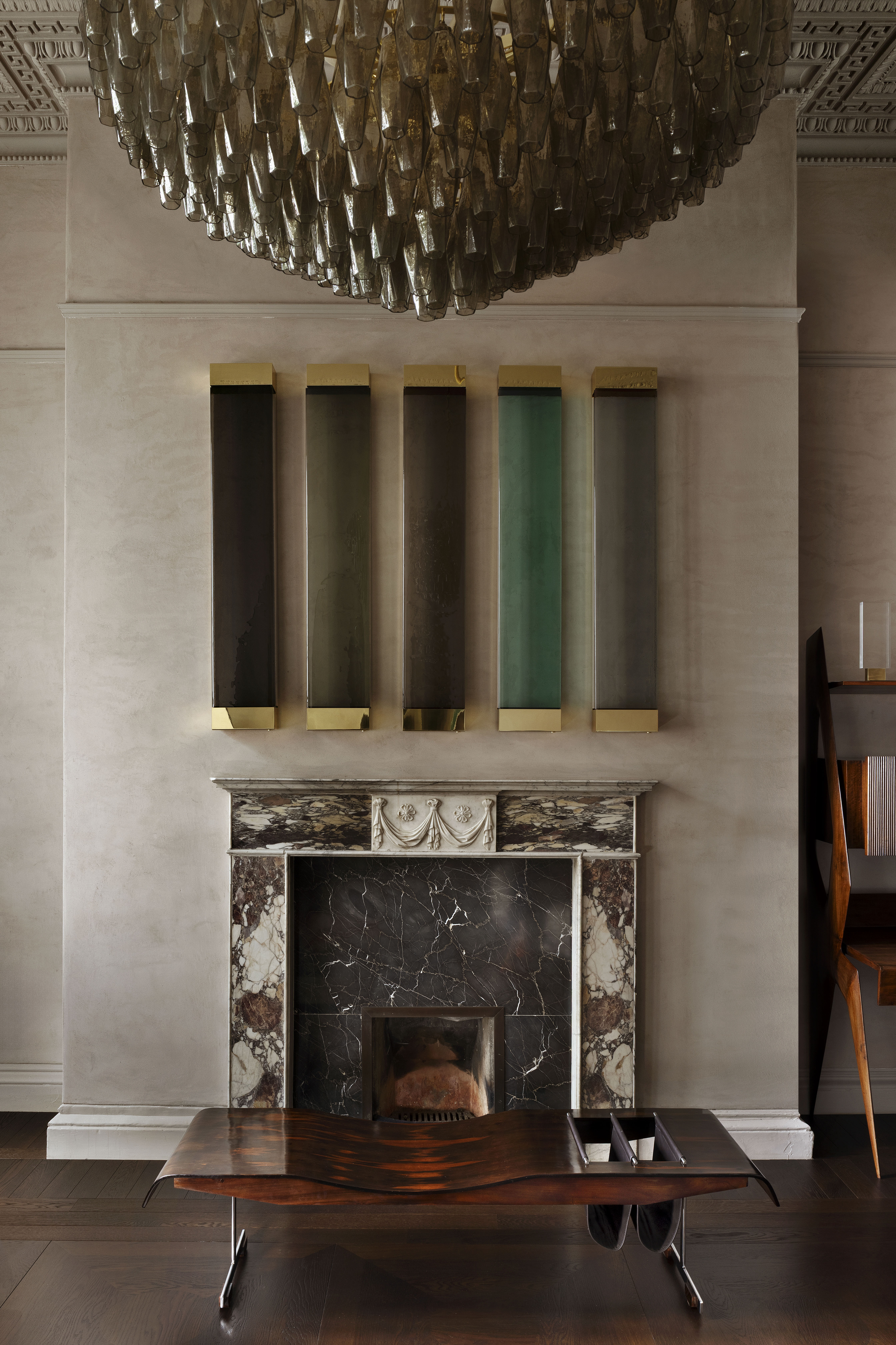 A chandelier made of glass elements, a black marble fireplace, a wooden coffee table, and an accent wall with five rectangular panels.