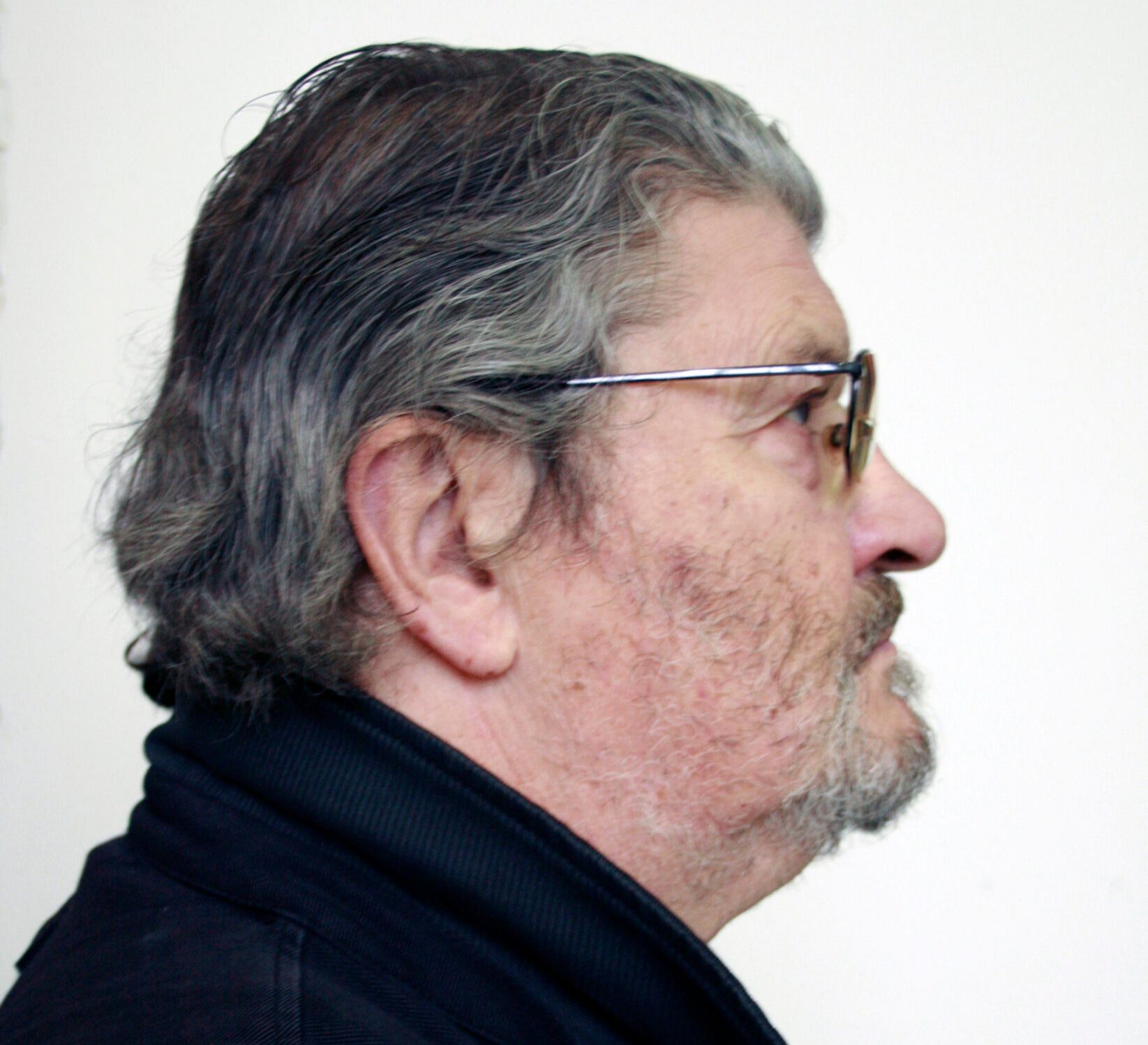 Portrait of David Harding with gray hair and beard, wearing glasses and a black jacket, looking right.