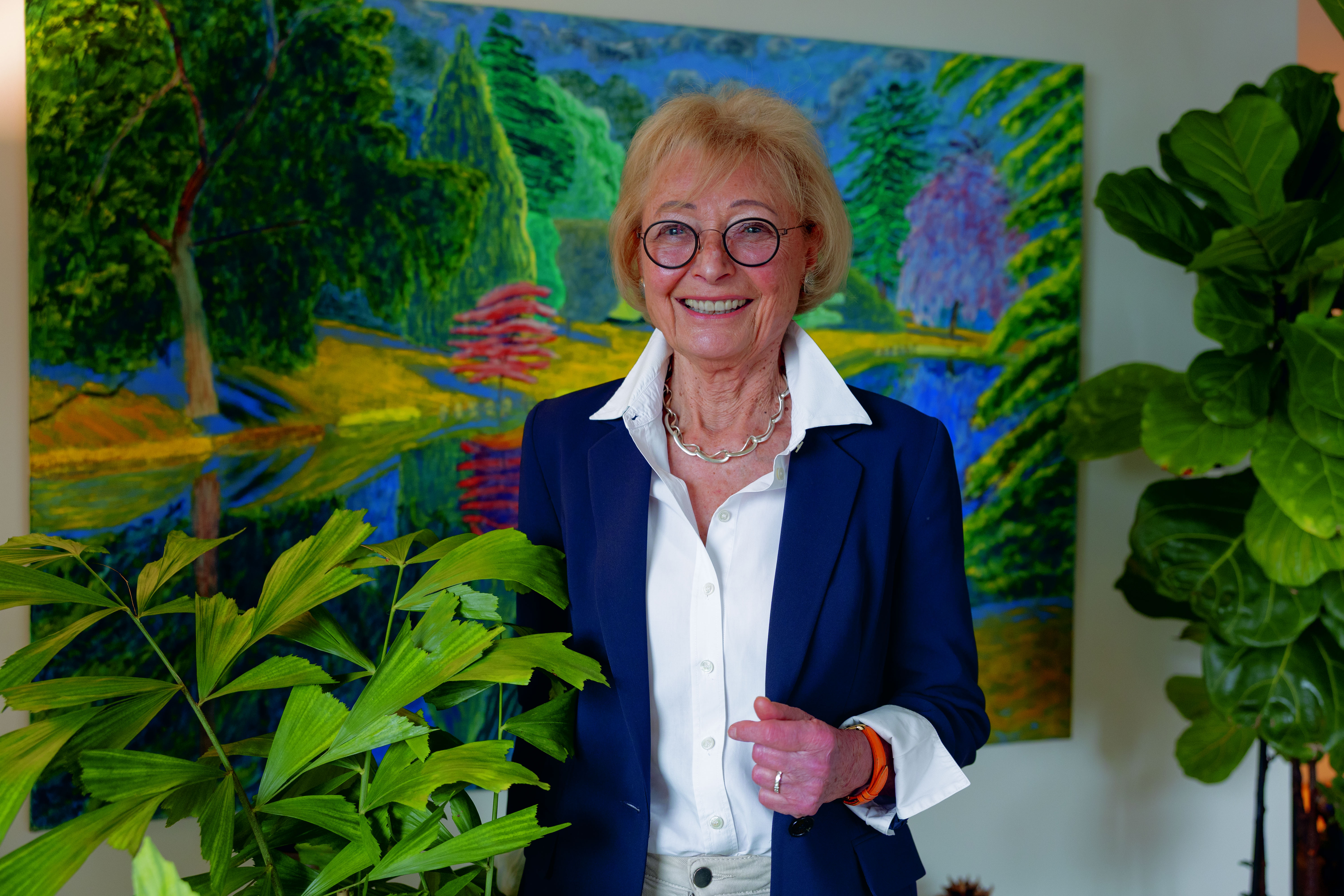 Helga Sands, an 88-year-old biohacker, stands in a room with a colorful landscape painting behind her.