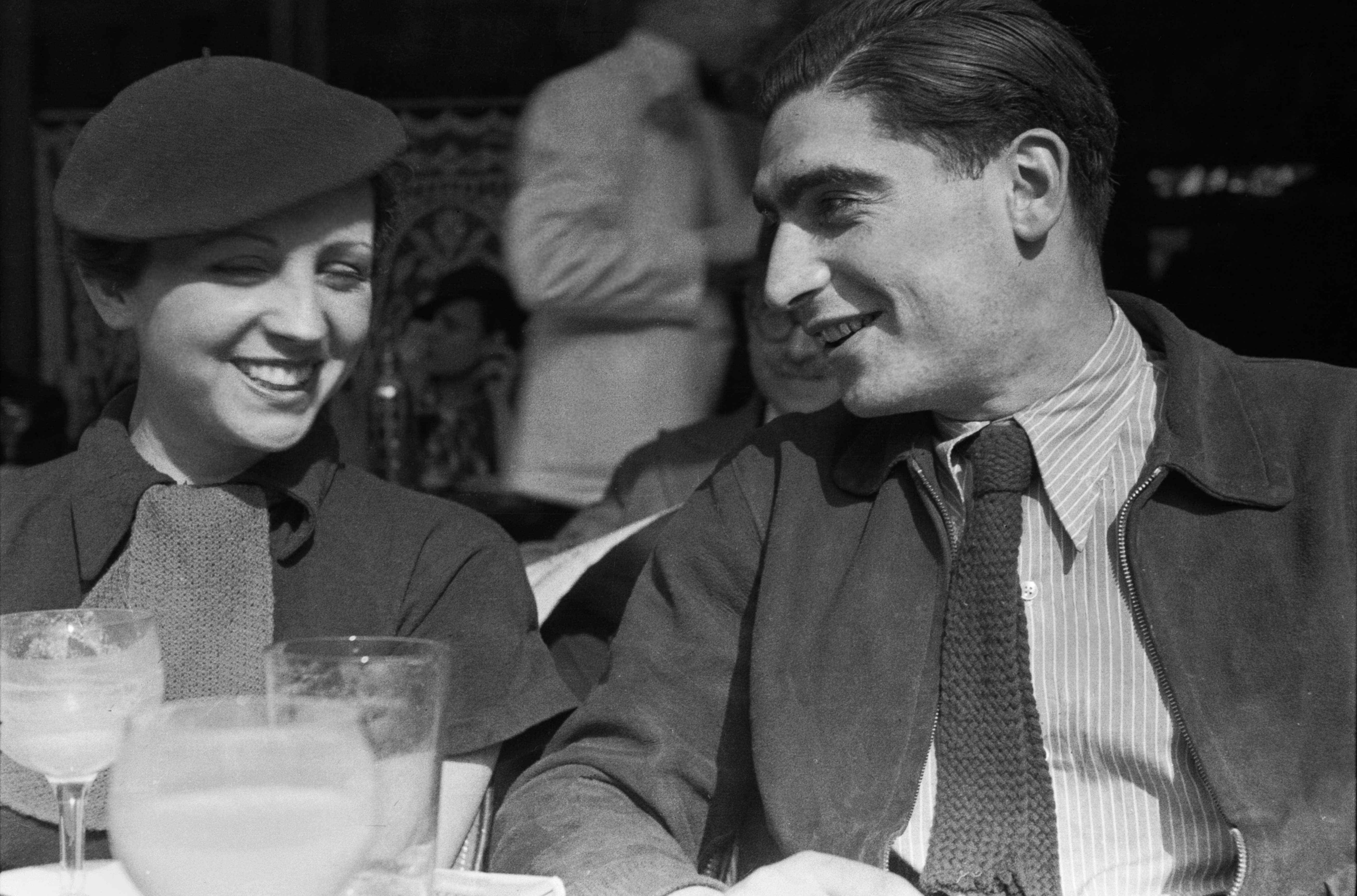 Gerda Taro and Robert Capa laughing at a sidewalk cafe.