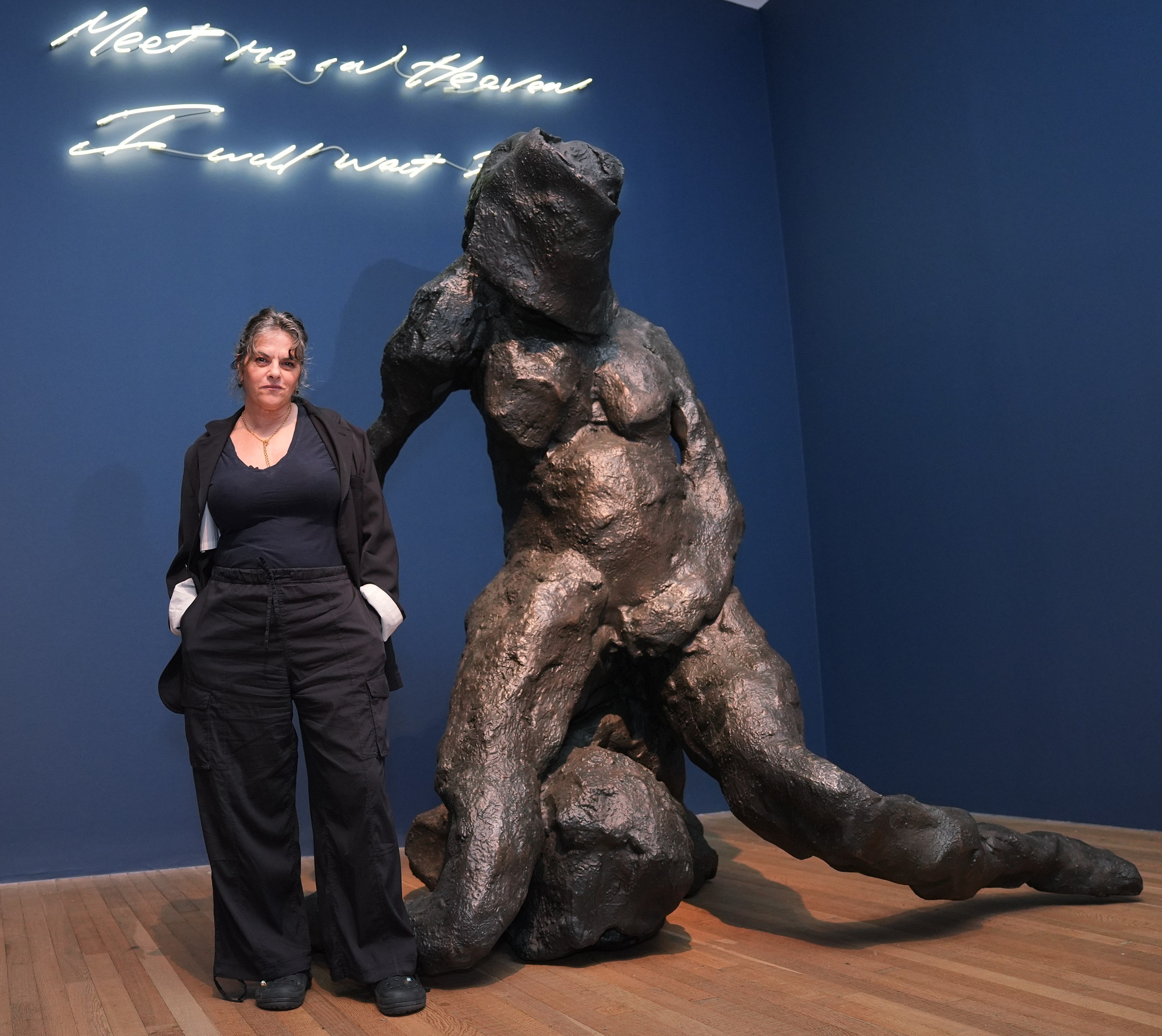 Tracey Emin stands next to her artwork "I Will Not Be Alone," a bronze sculpture, and a neon sign "Meet Me In Heaven I Will Wait For You."