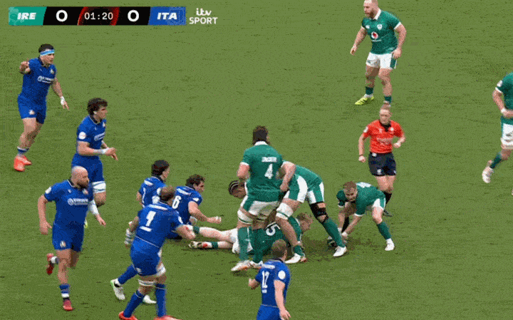 Rugby players in green and blue uniforms compete on a green field.