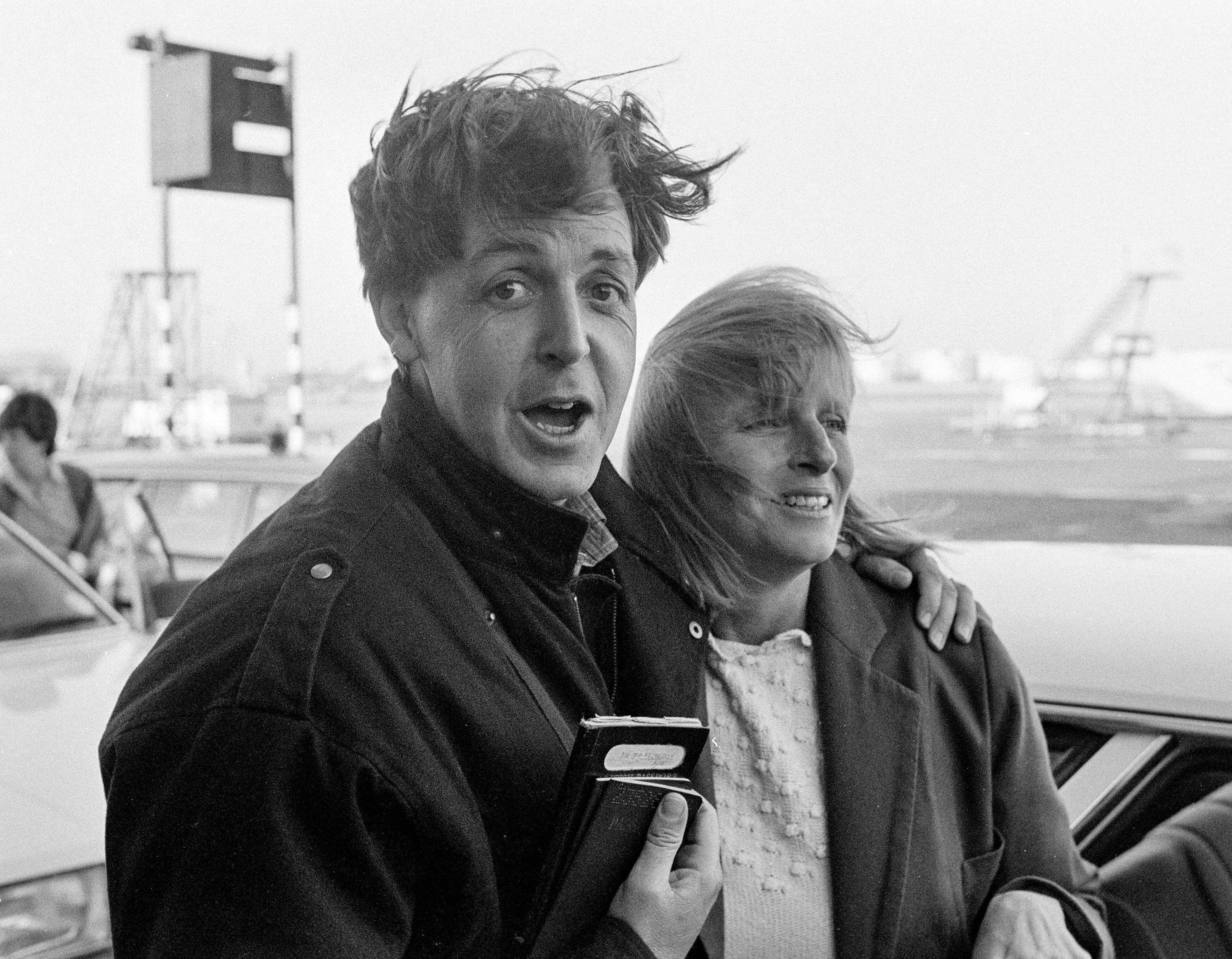 Paul McCartney and Linda McCartney with windblown hair at an airport.