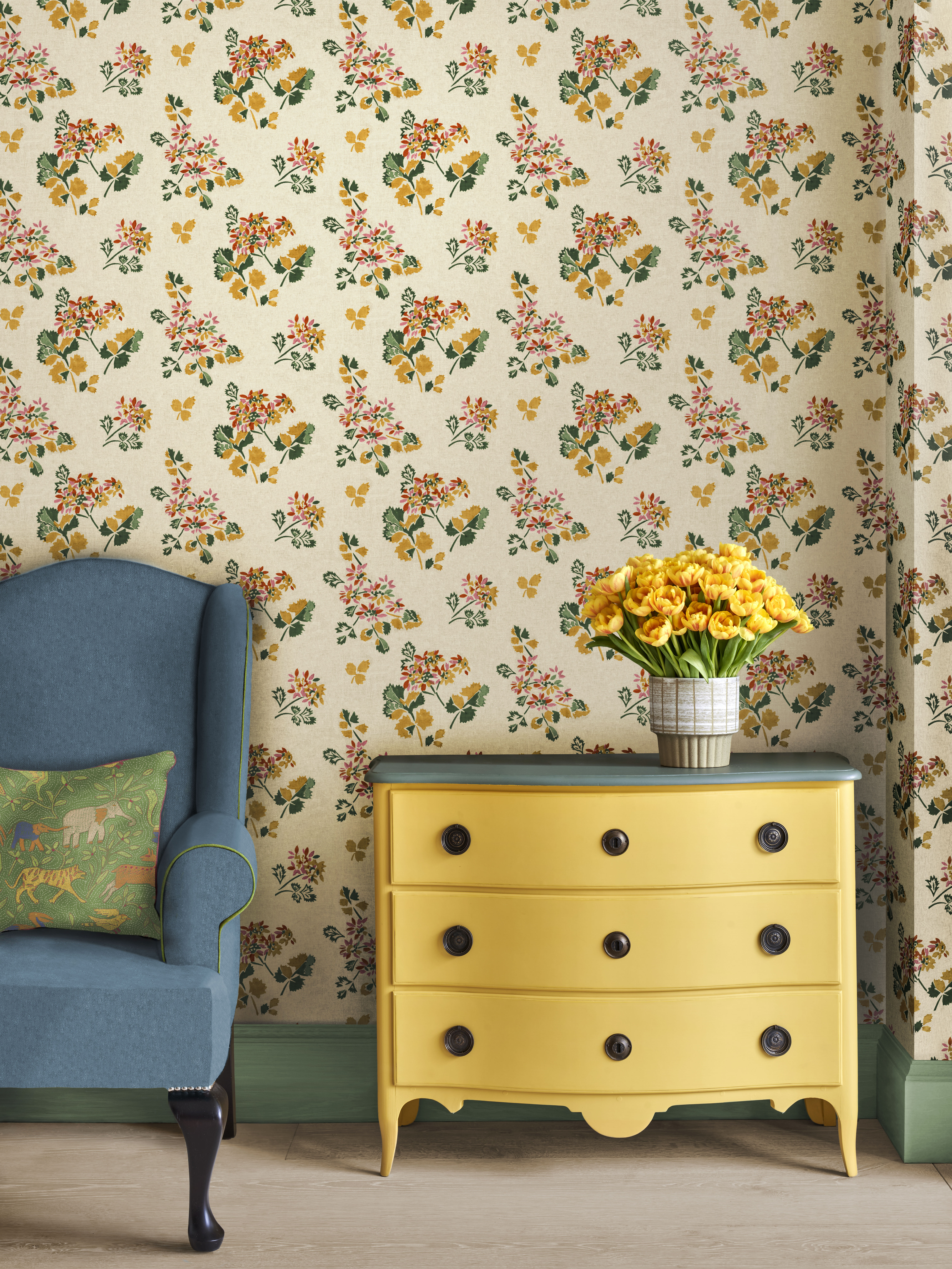 A blue armchair with a green elephant-patterned pillow next to a yellow dresser, both against a floral wallpaper.