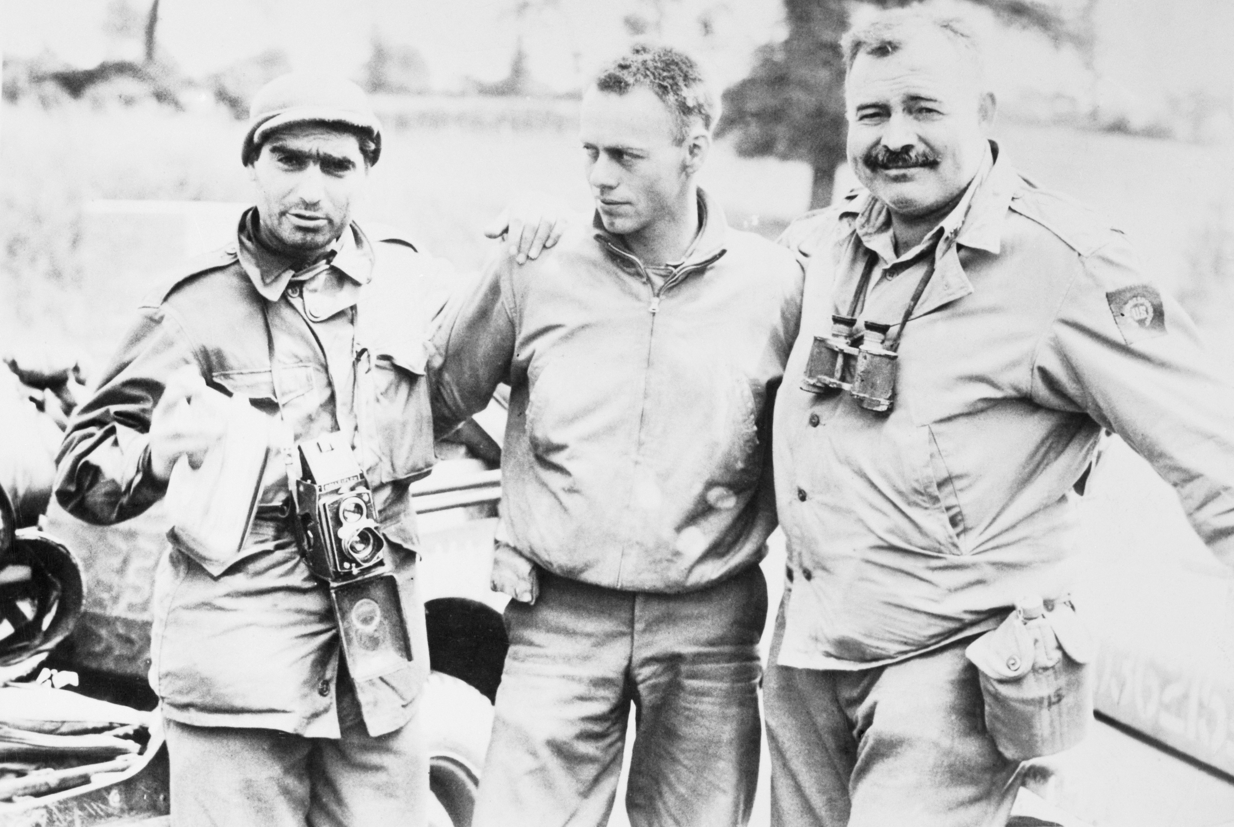 Life magazine photographer Robert Capa, an unidentified soldier, and author Ernest Hemingway stand together.