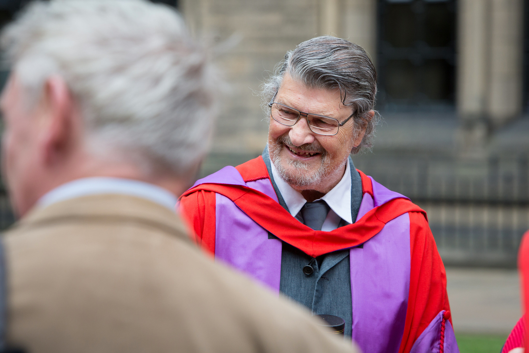 David Harding smiling while wearing academic regalia after receiving an honorary doctorate.