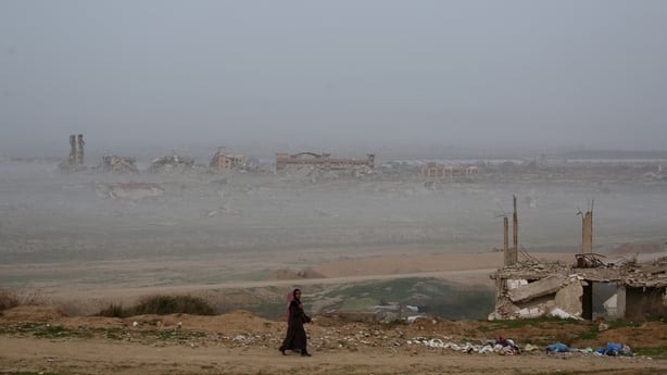 People walk next to destroyed buildings