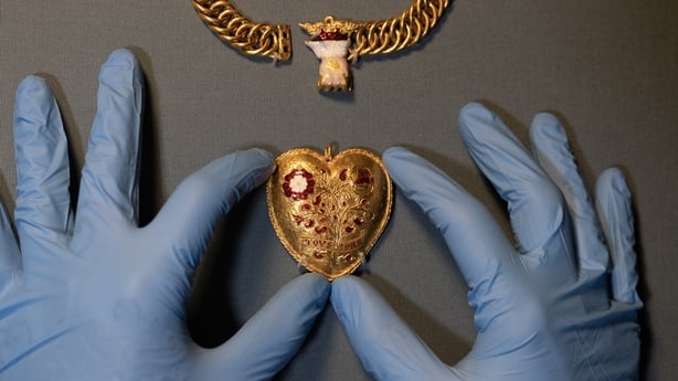 Blue gloved hands on either side of a gold pendant 