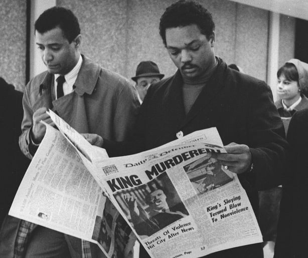 Black and white photo shows jesse jackson reading a newspaper with the front page headline 'King murdered'