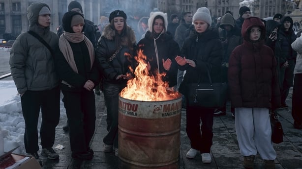 people stand around a fire in a barrel in freezing conditions