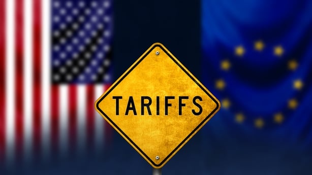 A yellow tariff sign in front of blurred EU and US flags