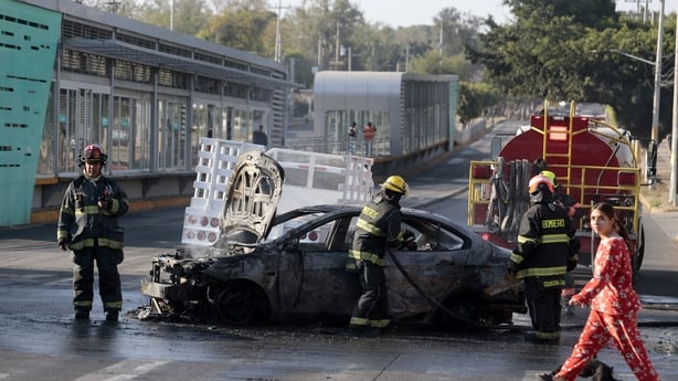 Firefighters extinguish a burning vehicle set on fire by organised crime groups in response to an operation in Jalisco to arrest a high-priority security target, at one of the main avenues in Zapopan, state of Jalisco, Mexico, on February 22, 2026. Armed civilians blocked several roads in the state