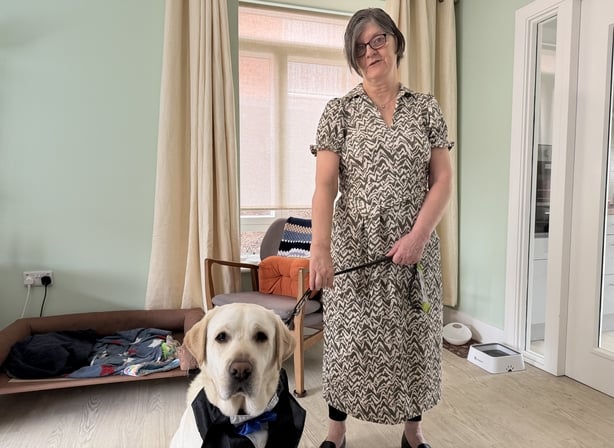 a woman wearing a floral dress holds the leash of a dog 