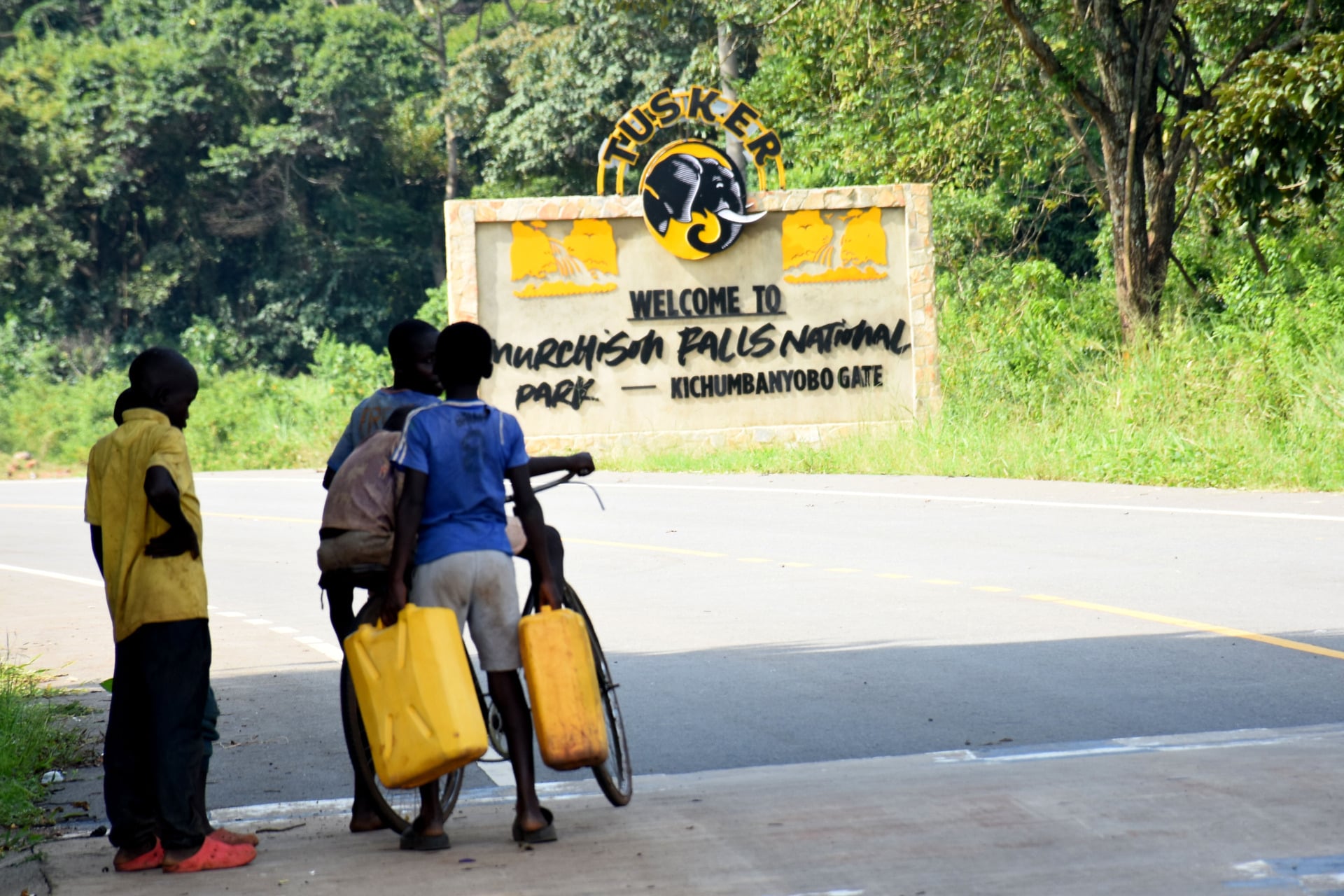 Two boys look as three others prepare to ride a bicycle with two jerrycans outside Murchison Falls National Park