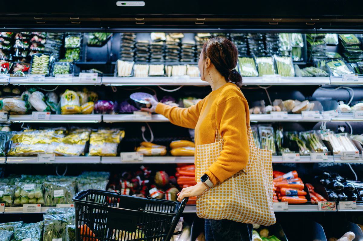 Young woman with shopping cart, carrying a reusable shopping bag, shopping for fresh organic fruits and vegetables in supermarket. Environmentally friendly concept. Zero waste and plastic free. Eco friendly shopping. Sustainable living lifestyle