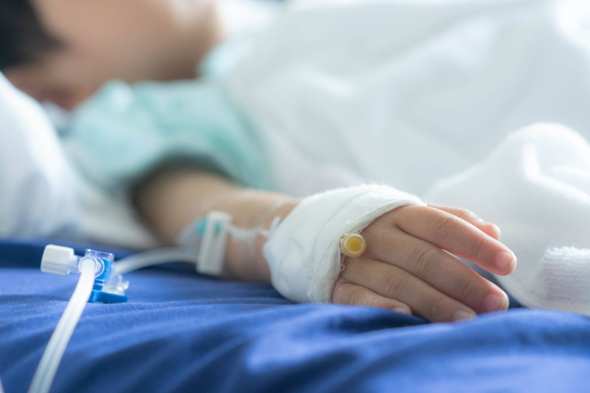 An individual in a hospital bed, resting with an arm featuring an intravenous line and a bandaged wrist, signifying medical care.