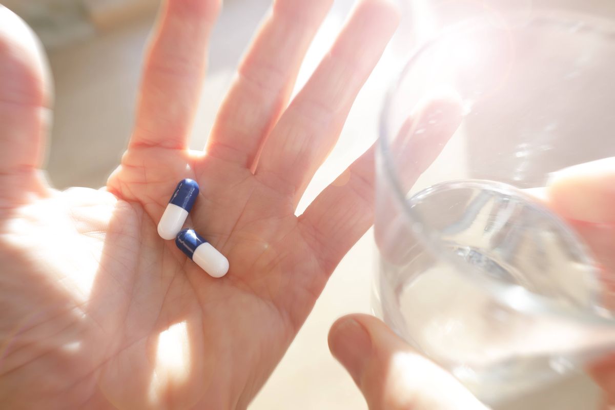 Hand containing medication with glass of water