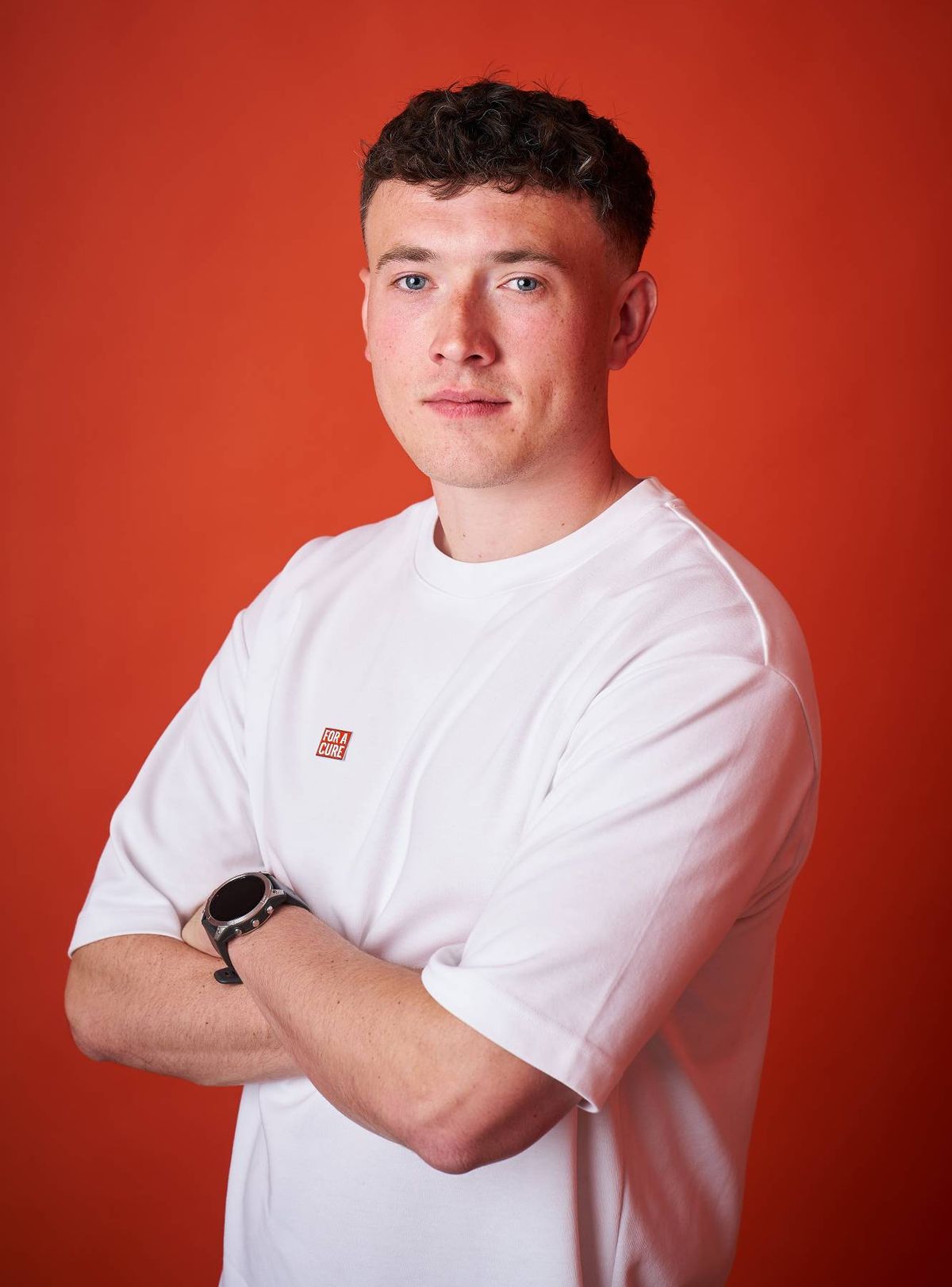 A person wearing a white t-shirt standing against a solid red background, looking straight into the camera with a neutral expression.