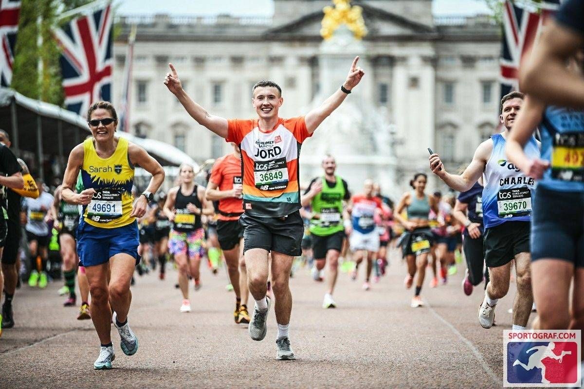 Participants in a marathon race, with one runner raising their arms in celebration, while others compete in front of a large, ornate building adorned with flags.