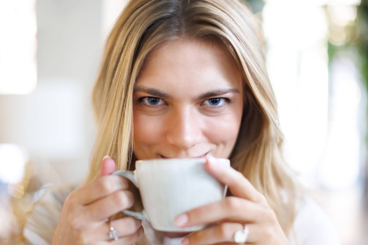 A close-up shot of a woman enjoying a cup of coffee, her eyes gleaming with pleasure and intimacy in a softly lit setting.