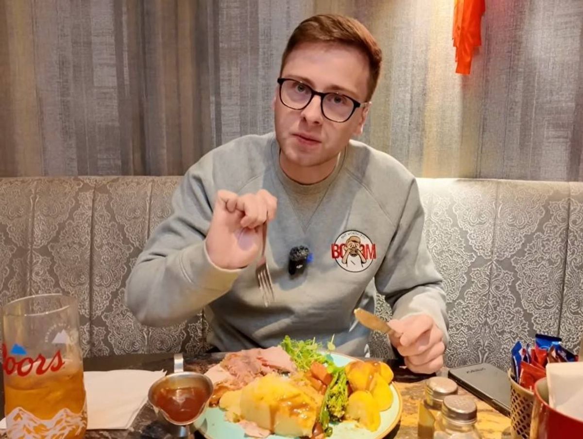 An individual, dressed in a gray long-sleeved shirt and wearing glasses, is seated at a table within a dining establishment, actively engaged in the consumption of a meal.