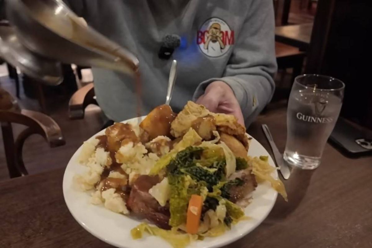 A person is adding a liquid to a plate of mixed vegetables and what appears to be a root vegetable, possibly served at a dining table.