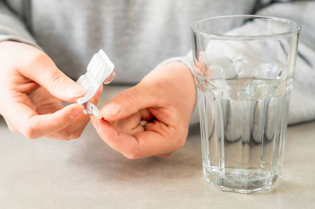Close-up on a woman's hands as she takes tablets from a blister pack, with a glass of water ready.