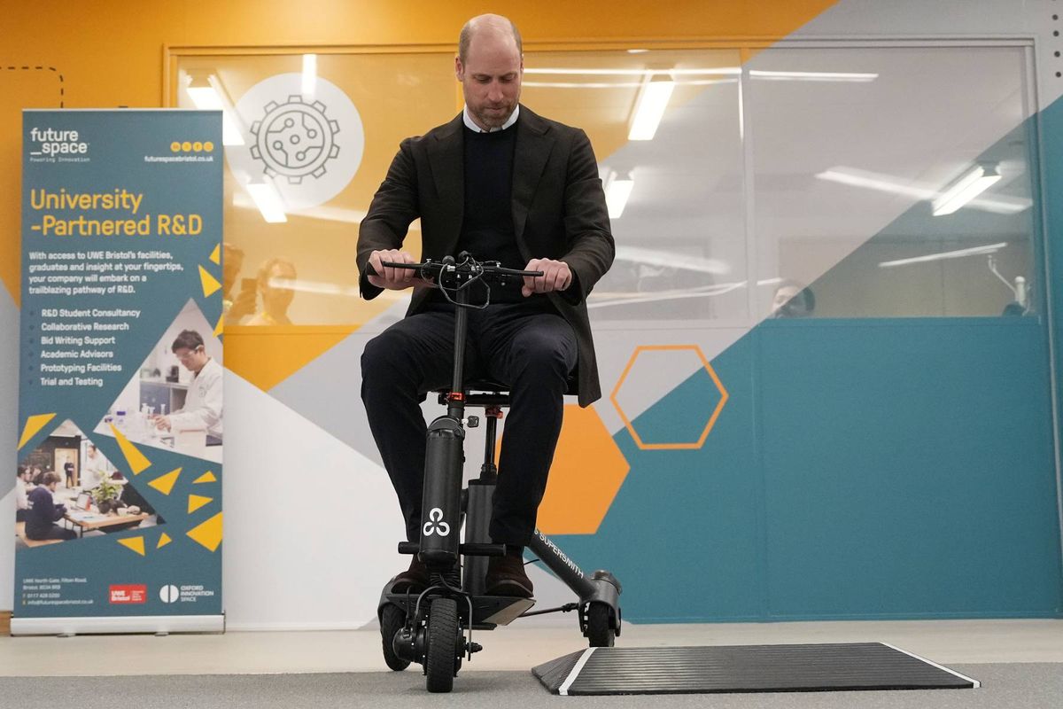 An individual is demonstrating the use of a modern, compact exercise bike inside a well-lit room, adorned with contemporary decor and promotional materials in the background.