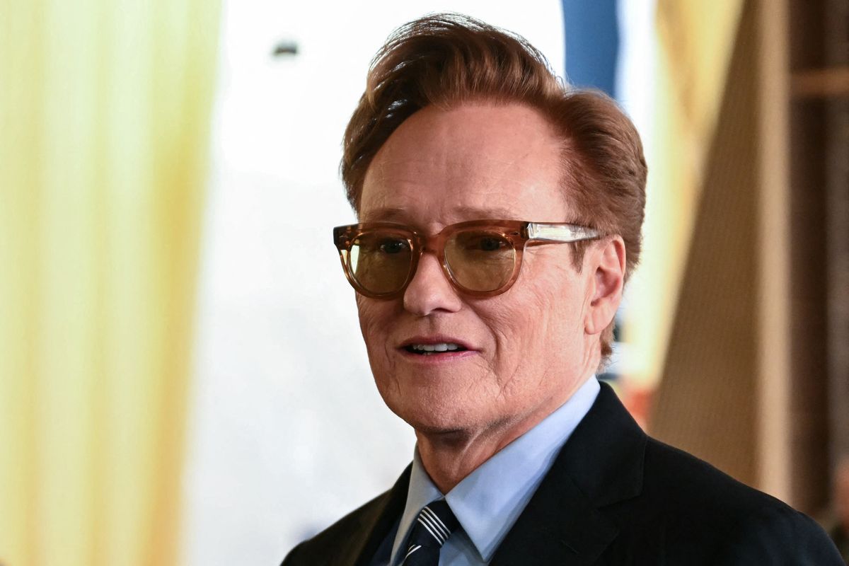Conan O'Brien wearing a blue shirt, tie, black jacket and brown sunglasses