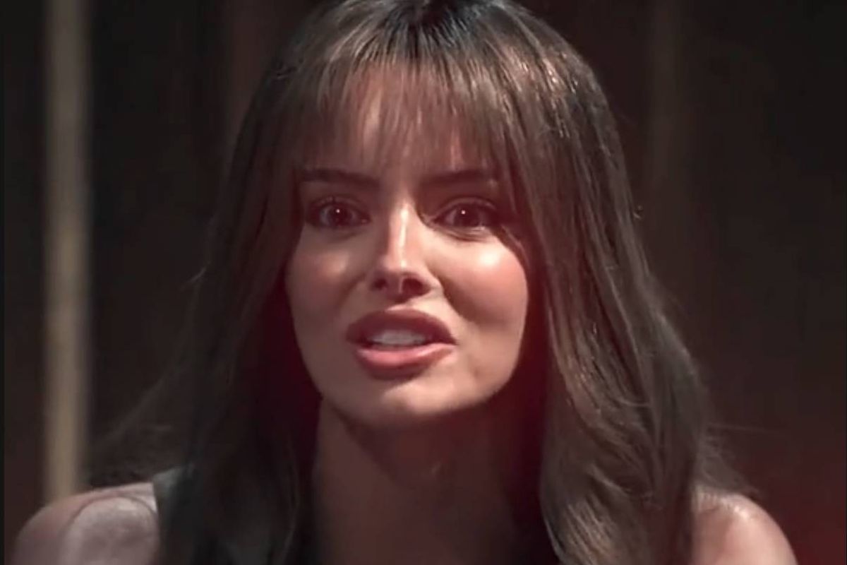 A close-up of an individual with long, straight hair, gazing intently into the camera with a slightly open mouth, positioned against a dimly lit background.