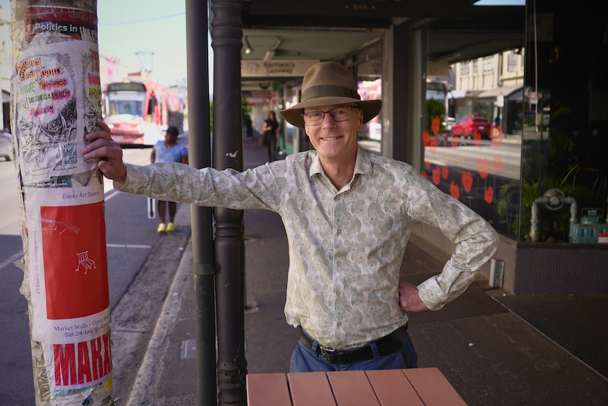 Brunswick Greens MP Tim Read stands smiling in his electorate, leaning against a pole.