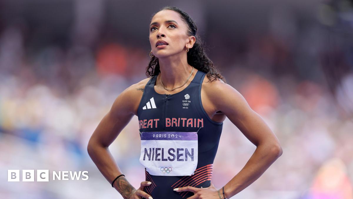 Laviai is stood with her hands on her hips looking up. She is wearing a GB navy tight fitting running vest. The words Great Britain are printed in red on her chest. She has a name tag with Nielsen on her front. She has dark brown curly hair tied off her face.