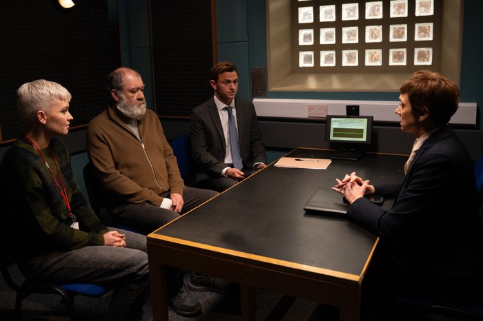 A solicitor and a welfare opposite sit either side of Bear in a police interview room, across from DS Walsh in a scene from Emmerdale