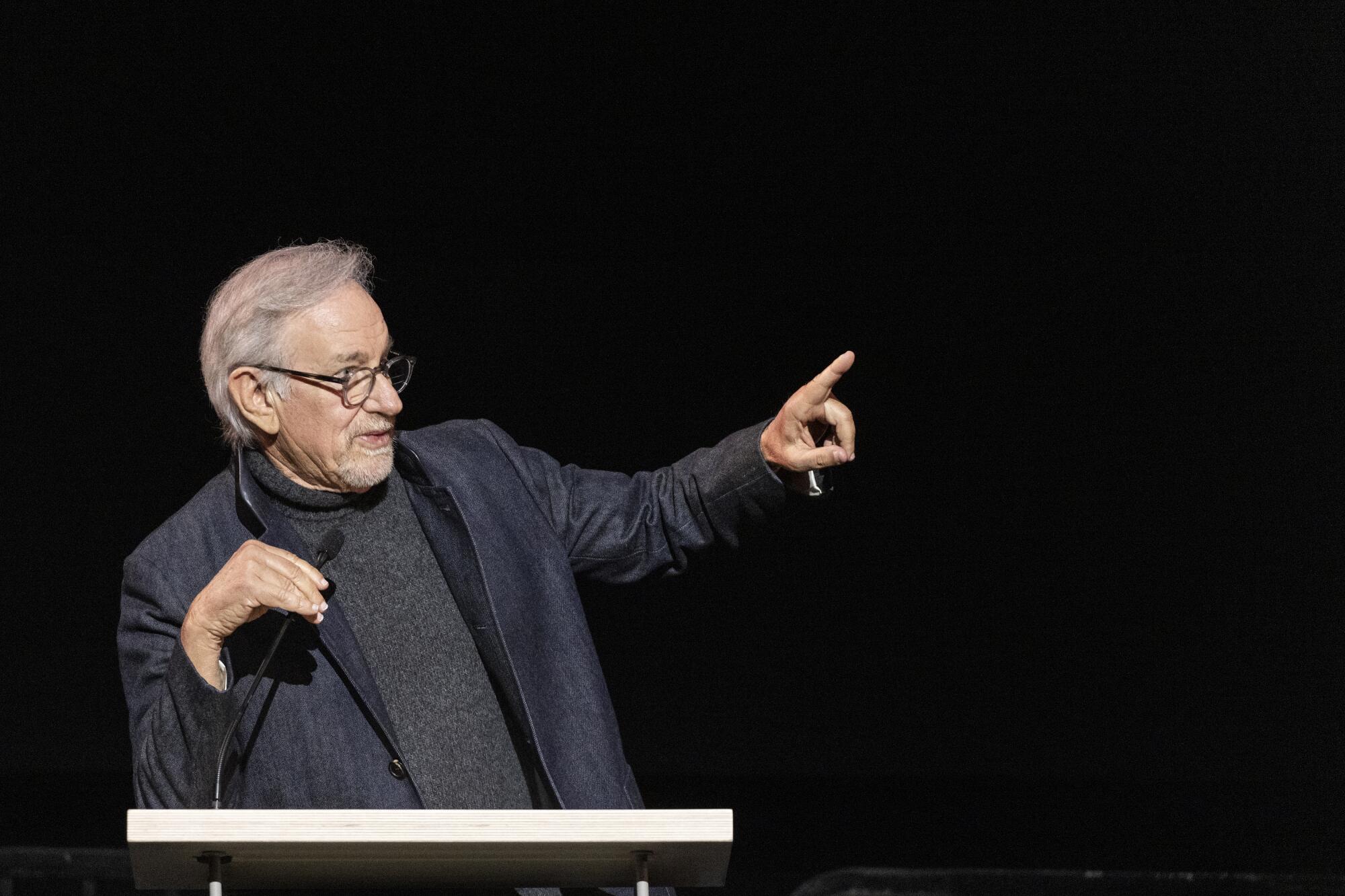 Steven Spielberg stands behind a microphone and points