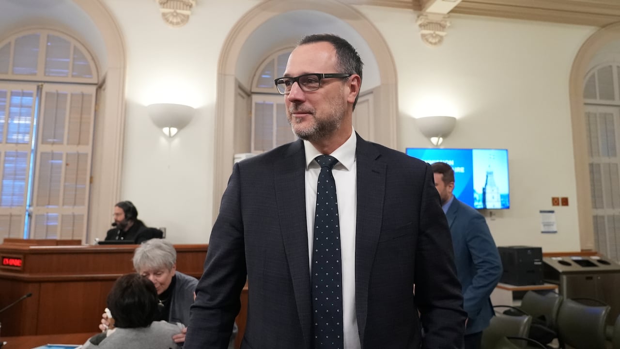 A man with a tie walks into a room, smiling.
