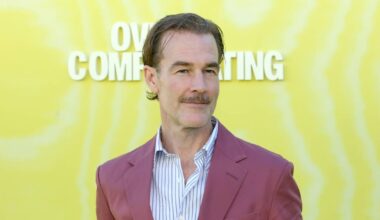 An individual dressed in a burgundy suit and light blue shirt stands against a bright yellow backdrop, likely at a public event or premiere. The background features the text "COMING" and "COM" in white font.
