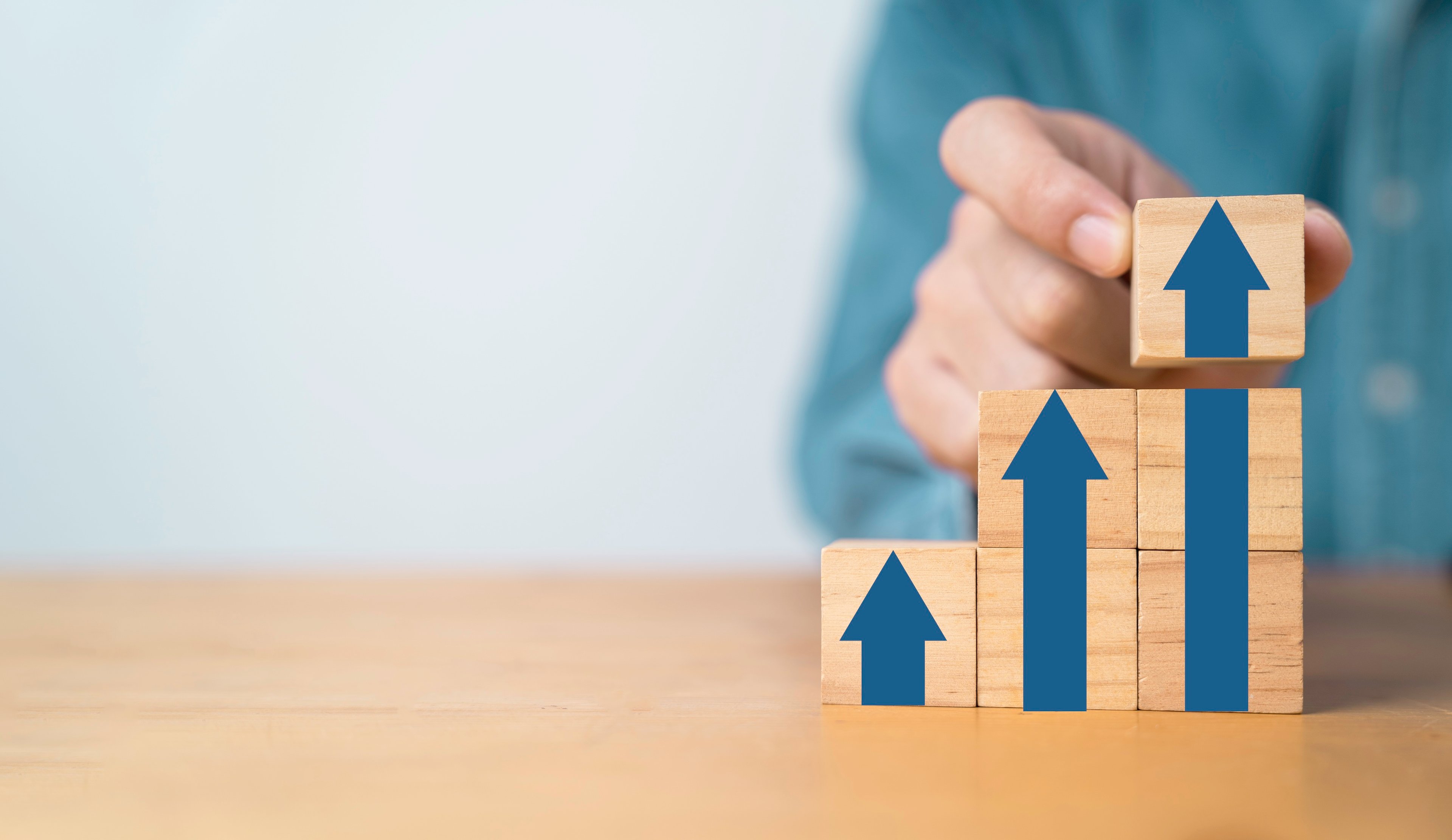 A person arranges building blocks to show increasingly large arrows that point up.